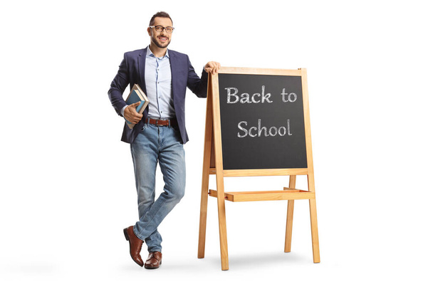 Full length portrait of a male teacher standing next to a blackboard with text back to school isolated on white background - Valokuva, kuva