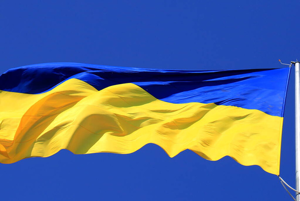 Σημαία της Ουκρανίας κυματίζει στον γαλάζιο ουρανό. Μεγάλη κίτρινη μπλε ουκρανική εθνική σημαία, πόλη Κίεβο. Ημέρα Υπερασπιστή Σύνταγμα Ανεξαρτησίας της Ουκρανίας - Φωτογραφία, εικόνα