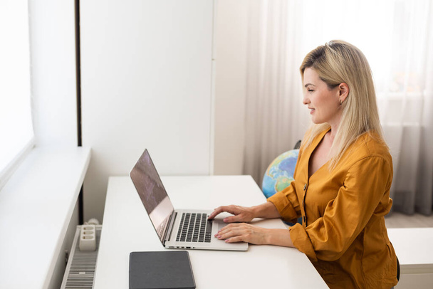 Εικόνα mockup μιας γυναίκας που χρησιμοποιεί και πληκτρολογεί σε laptop με λευκή οθόνη γραφείου σε ξύλινο τραπέζι - Φωτογραφία, εικόνα
