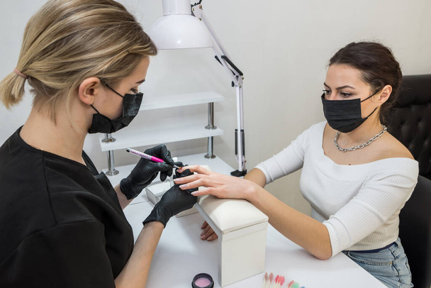 The manicurist applies a base layer to the client's nail.Applying a transparent varnish with a brush.The alignment of the nail plate with nail Polish.Professional  manicure in a beauty salon. - Valokuva, kuva