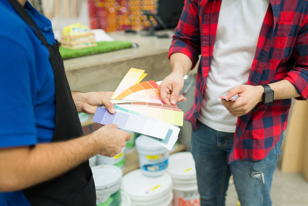 Close up of a hardware store employee showing the color swatches to a young man shopping for paint  - Fotografie, Obrázek