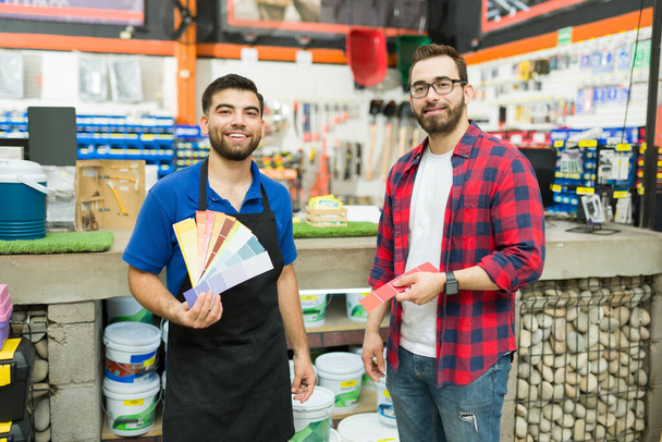 Portrait of a happy hardware store worker and young man or customer showing the color paint swatches while shopping - Fotoğraf, Görsel