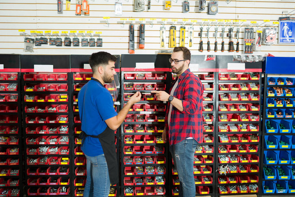 Hardware store worker showing different screws to a young man client looking to buy tools - Photo, image