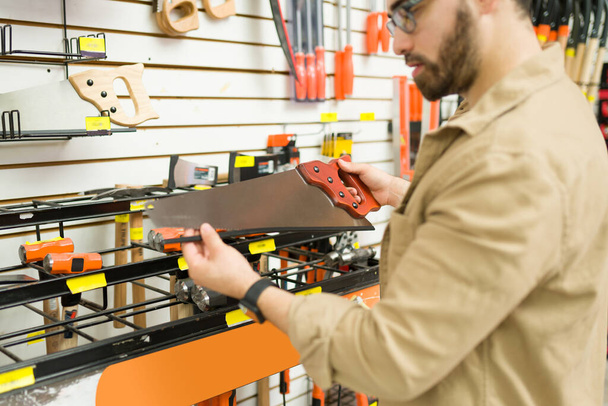Close up of a young man and customer looking at the tools at the hardware store and buying a new saw - Foto, imagen