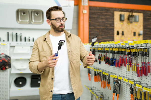 Attractive young man shopping at the hardware store making a decision and choosing to buy a new screwdriver - Foto, immagini