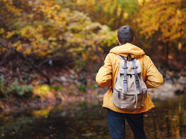 Travel and road trip concept at autumn. Adventure and active lifestyle in nature. Tourist hiking in forest. Caucasian man in yellow jacket walks in woods. - Foto, imagen