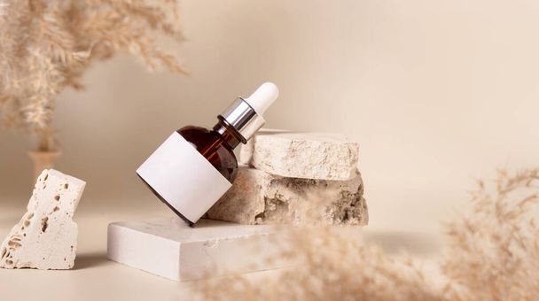 Brown dropper bottle with blank label on travertine stone near dry pampas grass on light yellow, close up, mockup. Skincare beauty product. Natural cosmetics. Boho compositio - Fotografie, Obrázek