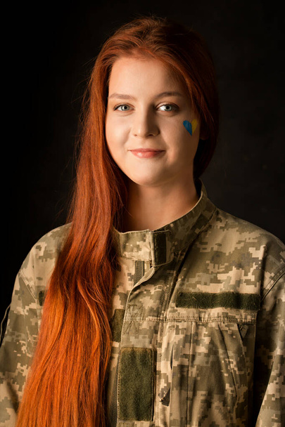 A young woman in camouflage with a blue and yellow heart on her face. Symbol of victory of Ukraine - Foto, Bild