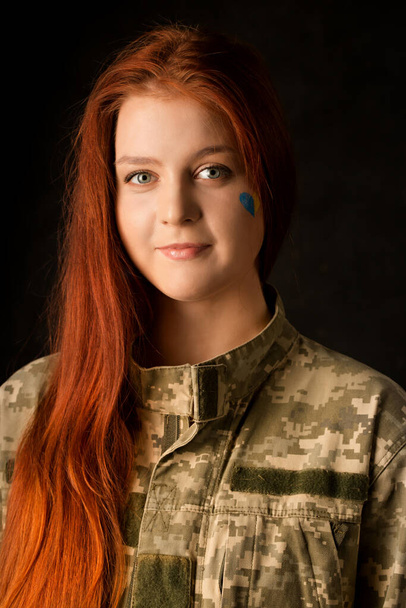 Молодая женщина в камуфляже с голубым и желтым сердцем на лице. Символ победы Украины - Фото, изображение
