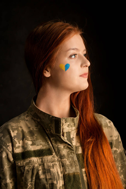 A young woman in camouflage with a blue and yellow heart on her face. Symbol of victory of Ukraine - Fotoğraf, Görsel