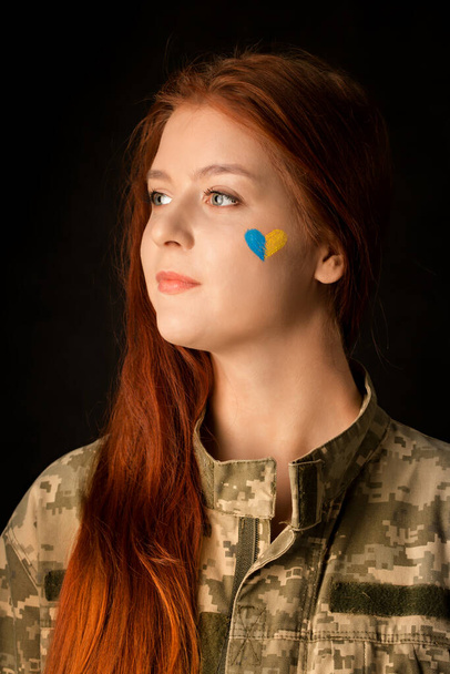 Молодая женщина в камуфляже с голубым и желтым сердцем на лице. Символ победы Украины - Фото, изображение