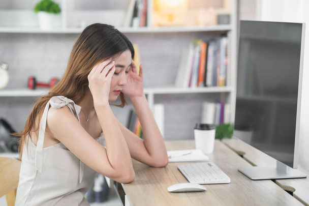Азійська бізнес-жінка переживає важкі депресії під час роботи на ноутбуці або комп'ютері на дерев'яному столику у себе вдома. Сумний серіали про депресію, які працюють з будь - якого місця.. - Фото, зображення