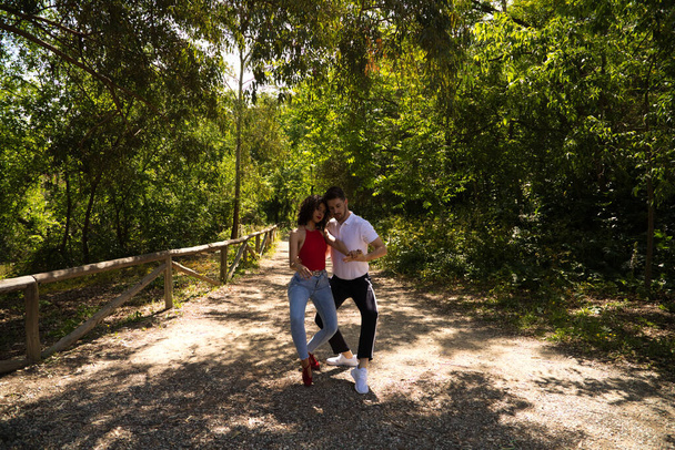 Красивый молодой человек и женщина танцуют бачату и сальсу в парке. Пара страстно танцует в окружении зелени. Концепция танцев. - Фото, изображение