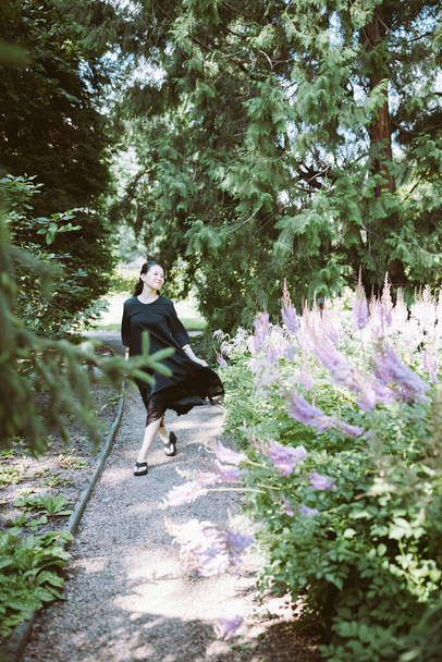 Beautiful happy middle-aged Japanese woman in black casual dress and wedge heel flip flops summer park, smiling. Sunlight, copy space - Fotoğraf, Görsel