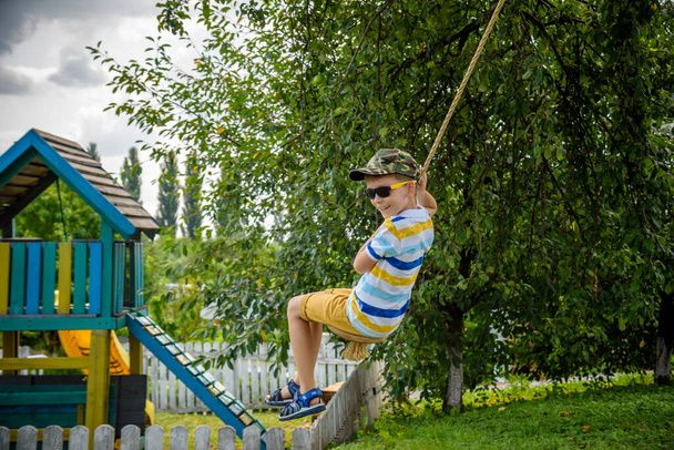 Щасливий маленький хлопчик розважається на мотузці, яку він знайшов, відпочиваючи за містом. Активний відпочинок з дітьми
. - Фото, зображення
