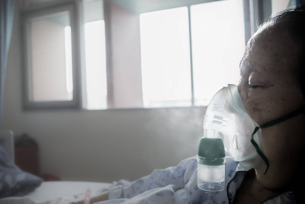 Азиатская пожилая пациентка госпитализирована и проходит респираторное лечение с использованием туманности на больничной койке - Фото, изображение