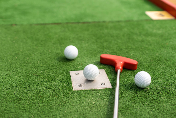Assorted miniature golf putters and balls askew on synthetic grass - Foto, Imagen