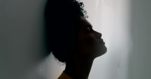 Silhouette fiatal fekete nő támaszkodik a falra. Töprengő afrikai lány - Felvétel, videó