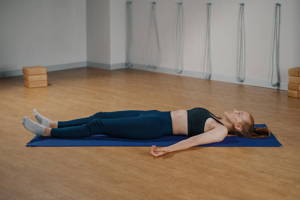 Женщина отдыхает во время йоги пилатеса, растягиваясь, лежа на полу. Возможно, девочка умерла во время занятий спортом - Фото, изображение
