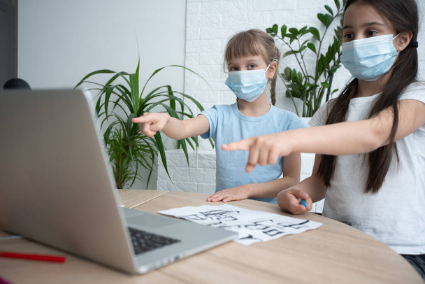 dos niña pequeña estudiando en línea y trabajando en el ordenador portátil en el uso de la máscara facial. - Foto, Imagen