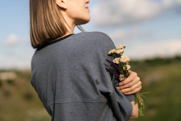 Happy people. Cropped image of a smiling woman holding in her hand fresh field flowers - Photo, image