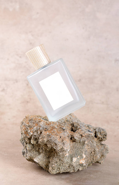 Transparent bottle of perfume with white labels on stone podium on beige terracotta background with dry flower. Fragrance presentation, Minimal cosmetic packaging mockup, copy space - Photo, image