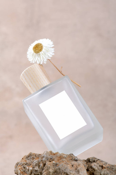 Balanced transparent bottle of perfume with white labels on stone podium on beige terracotta background with dry flower. Fragrance presentation, Minimal cosmetic packaging mockup, copy space - Photo, image