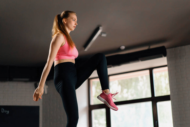 Athletic build girl doing endurance exercise training with leg swings in gym - Valokuva, kuva