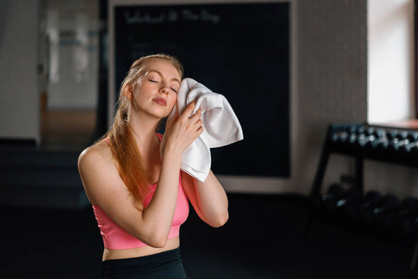 Athletic girl wipes sweat while relaxing after a grueling workout in gym - Fotografie, Obrázek