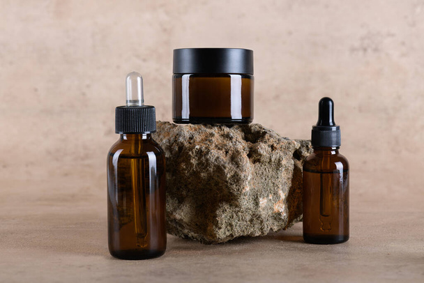 Group of amber glass bottle and jar mockup for moisturizer cream, serum, essensial on stone podium on beige background. Minimal cosmetic monochrome mockup for beauty product, cosmetic packaging mockup - Foto, Imagem
