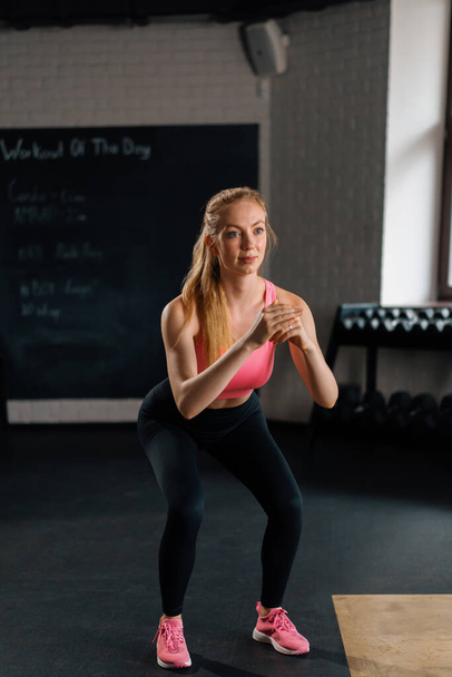 Athletic woman doing squat workout exercise in the gym - Fotó, kép