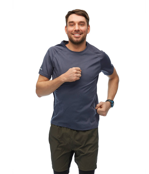 fitness, sport and healthy lifestyle concept - smiling man in sports clothes with smart watch or tracker running over white background - Photo, image