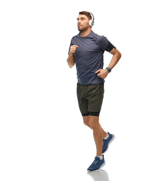fitness, sport and healthy lifestyle concept - man in headphones with smart watch or tracker running over white background - Photo, image