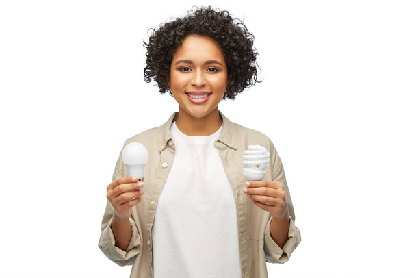 eco living, energy saving and sustainability concept - portrait of happy smiling woman comparing lighting bulbs over white background - Photo, Image