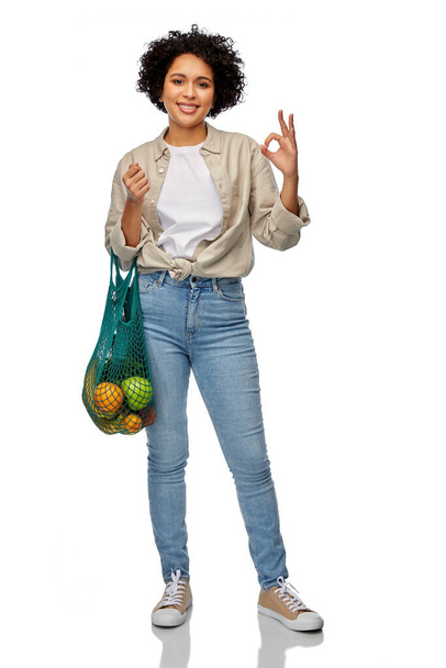 sustainability, food shopping and eco friendly concept - happy smiling woman holding reusable string bag with fruits and vegetables showing ok gesture over white background - Foto, Bild