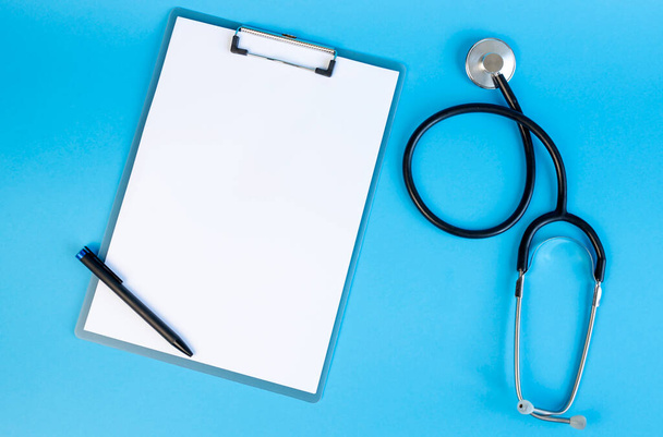 Stethoscope και πρόχειρο με λευκό λευκό φύλλο χαρτιού και στυλό, σε μπλε φόντο. Θέση για κείμενο - Φωτογραφία, εικόνα