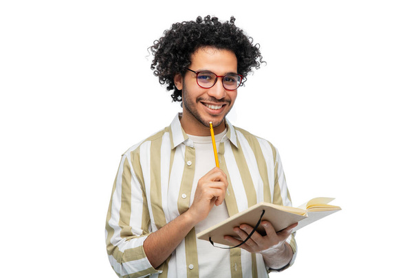 freedom, motion and happiness concept - happy smiling young man in glasses with diary and pencil writing over white background - Фото, зображення