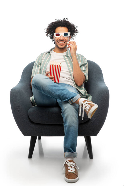 cinema, leisure and entertainment concept - happy smiling young man in 3d glasses with popcorn sitting in chair over white background - Fotó, kép
