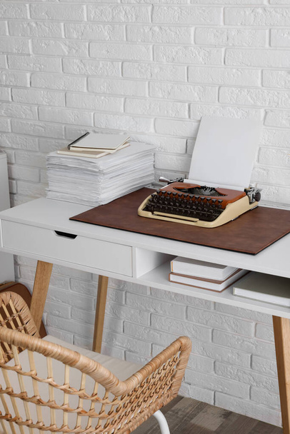 Зручне робоче місце письменника з друкарською машинкою на столі біля білої цегляної стіни
 - Фото, зображення