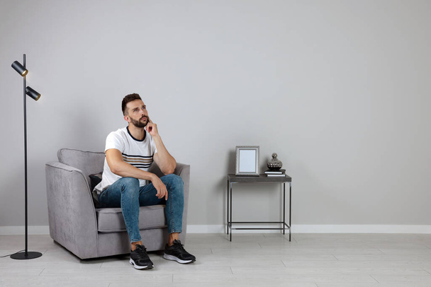 Man sitting in armchair near gray wall, space for text - Foto, afbeelding