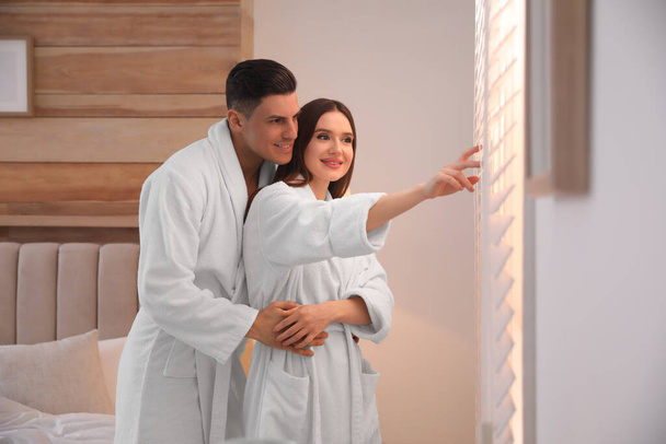 Happy couple wearing bathrobes near window in bedroom - Zdjęcie, obraz