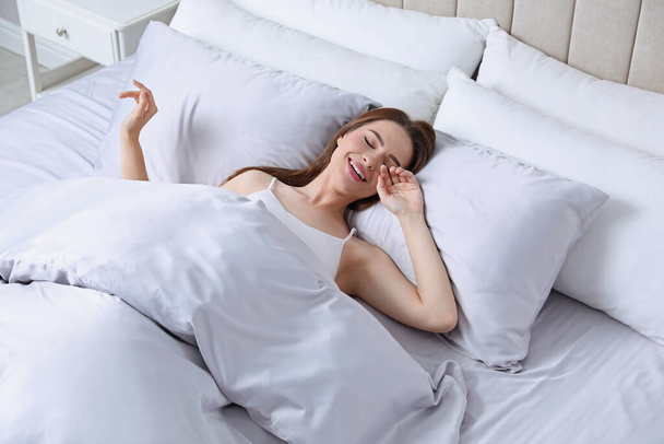 Young woman awaking in comfortable bed with silky linens - Foto, Bild