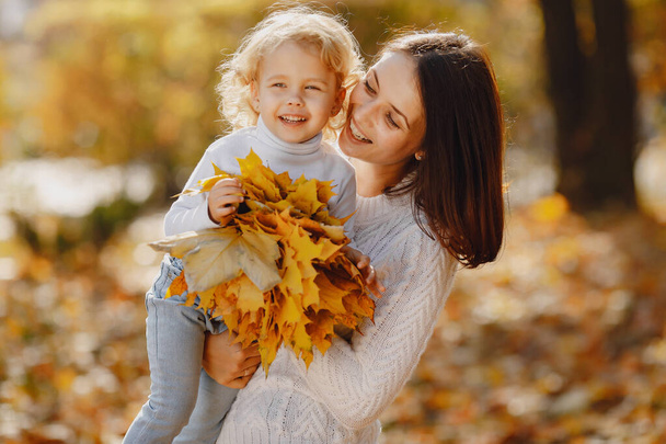 Fashionable mother with daughter. Family in a autumn park. Little girl in a white sweater. - 写真・画像