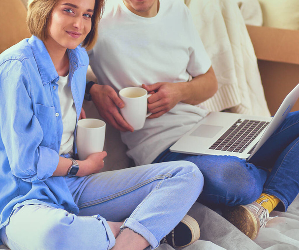 Couple buying online with a laptop and moving house sitting on the floor. - Foto, Bild