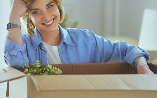 A beautiful single young woman unpacking boxes and moving into a new home. - Foto, Imagen