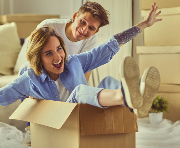 Счастливая пара веселится и катается в картонных коробках в новом доме. - Фото, изображение