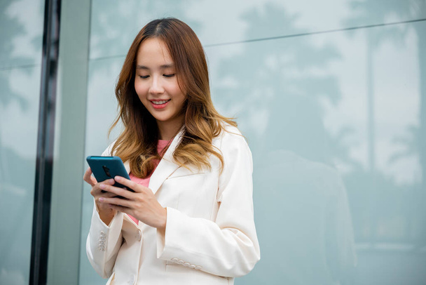 Asian businesswoman working with mobile phone standing against street front building near office, Portrait successful business woman smiling holding smartphone use application chat online in morning - Fotografie, Obrázek