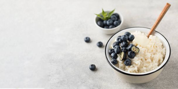 Rice milk porridge with blueberries in a bowl close-up on a grey background. The concept of a healthy and tasty breakfast. Copy space - Valokuva, kuva