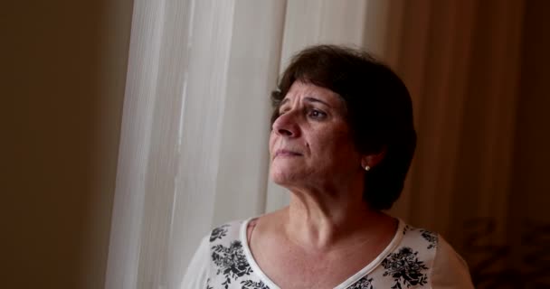 Contemplative senior woman looking through window, anxious depressed older lady - Filmati, video