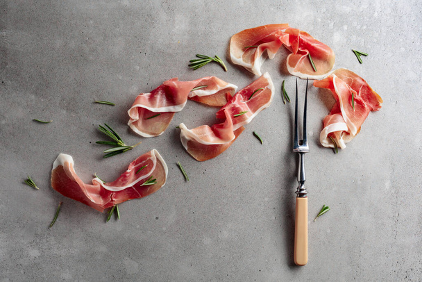 Prosciutto with rosemary on an old concrete background. Traditional Mediterranean snack. Top view. - Zdjęcie, obraz